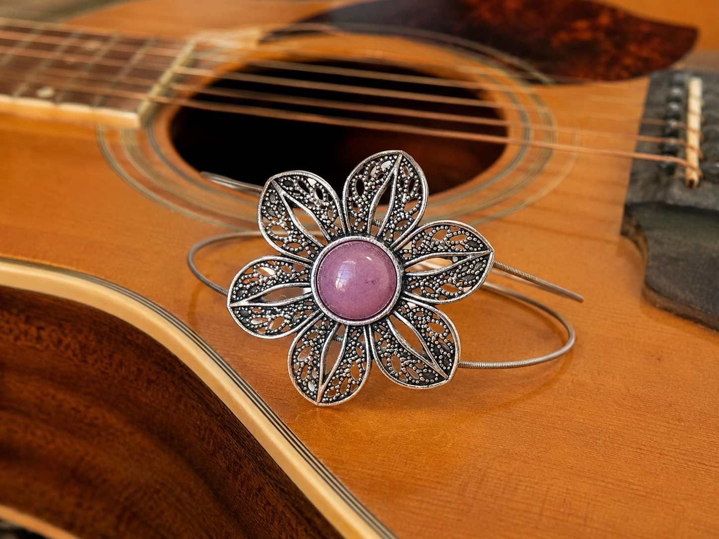 Silver flower-shaped bracelet with a pink center on an acoustic guitar