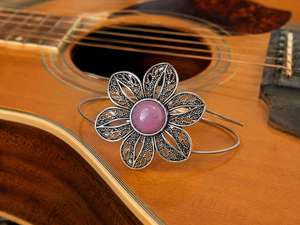 Silver flower-shaped bracelet with a pink center on an acoustic guitar