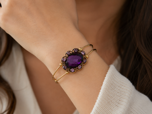 Gold bracelet with a purple gemstone worn on a wrist