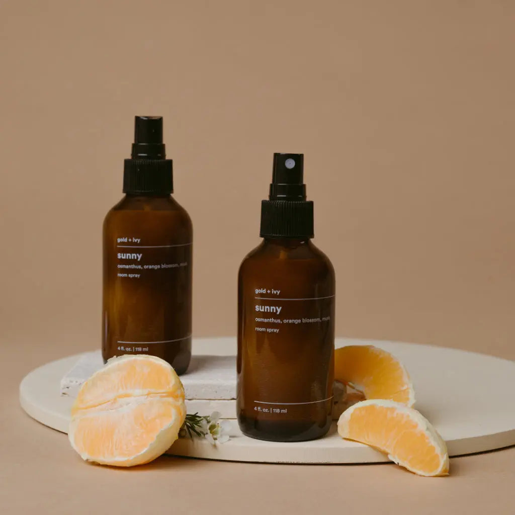 Gold + Ivy Sunny room spray in amber bottles with orange slices and white flowers