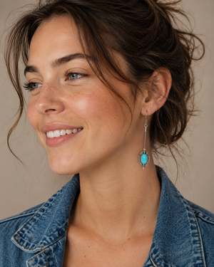 Woman wearing a blue denim jacket with turquoise earrings against a neutral background